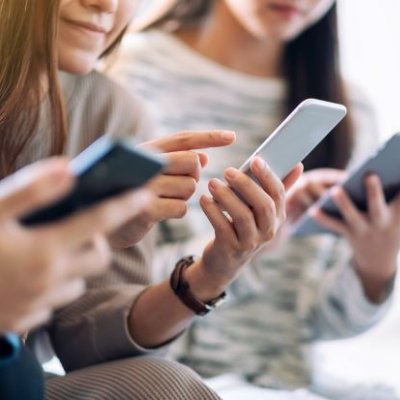 A group shot of three teenage girls looking down at mobile devices in their hands 